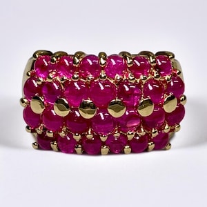 May include: A gold ring with a band of pink gemstones. The ring is set with multiple rows of round, bezel-set stones.