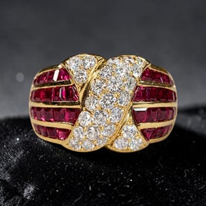 Puede incluir: Un anillo de oro con una banda diagonal central de diamantes blancos redondos de talla brillante, flanqueada por dos secciones de rubíes rojos oscuros de talla cuadrada engastados en canal, creando un patrón cruzado con oro pulido.