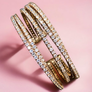 May include: A gold bangle bracelet with multiple rows of clear cubic zirconia stones.