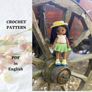 Puede incluir: Patrón de crochet PDF en inglés para una muñeca con piel morena, cabello negro, un sombrero amarillo, un top de crochet blanco, una falda de crochet verde y zapatos azules. La muñeca está de pie sobre una rueda de madera.