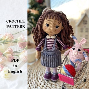 May include: Crochet pattern PDF in English for a brown haired doll wearing a purple and white checked shirt, a grey skirt, and brown shoes. The doll is holding a pink crocheted bunny in a miniature shopping cart with a colourful ball.