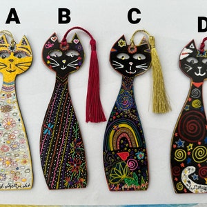 May include: Four hand-painted wooden cat bookmarks with colorful designs and tassels. The bookmarks feature different patterns, including flowers, swirls, and rainbows. The cats have black eyes and white whiskers.