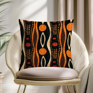 Può includere: Cuscino quadrato decorativo con sfondo nero e motivo astratto arancione, rosso e crema. Il design presenta linee ondulate verticali, cerchi e punti. Il cuscino è appoggiato su una sedia bianca.