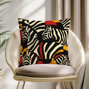 Può includere: Cuscino quadrato decorativo con un'audace stampa zebrata. Il cuscino presenta uno sfondo nero con strisce zebrate color crema, rosse e gialle. Il cuscino è posto su una sedia color crema.