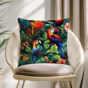 May include: Square throw pillow featuring a vibrant tropical design. The pillow showcases colorful parrots perched among lush green foliage, orange flowers, and pink blossoms. The pillow is placed on a woven chair with a neutral cushion.