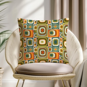 Può includere: Cuscino quadrato con un motivo geometrico retrò nei toni dell'arancione, verde e crema. Il cuscino è posto su una sedia intrecciata con una seduta colorata neutra, creando un'estetica moderna della metà del secolo.