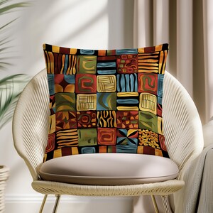 May include: Square throw pillow with a colorful patchwork design. The pillow features a variety of geometric shapes and patterns in shades of red, orange, yellow, green, blue, and black. The pillow is placed on a white chair.