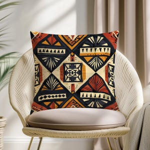 May include: Square cushion featuring a geometric design in black, orange, cream, and rust hues. The cushion is placed on a woven chair with a beige seat, offering a blend of comfort and style.