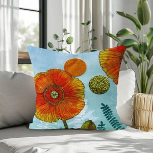 May include: Square throw pillow with a watercolor design featuring orange poppies and circular shapes on a light blue background. The pillow has a floral theme with green and white accents, perfect for home decor.