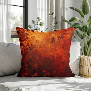 May include: A square throw cushion featuring a vibrant, abstract design of deep red, orange, and golden yellow hues. The surface displays a dense pattern of dark, silhouetted leaves and delicate vine-like branches that frame the edges of the fabric.