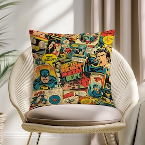 May include: Square throw pillow featuring a collage of vintage comic book panels. The design includes images of superheroes in action, speech bubbles, and bold colors like red, blue, and yellow. The pillow is placed on a white chair.