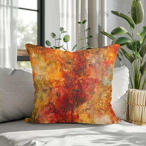 May include: A square throw cushion featuring an abstract, painterly design with vibrant layers of warm autumn colours including deep red, burnt orange, golden yellow, and hints of dark brown, resembling a dense forest canopy in autumn.