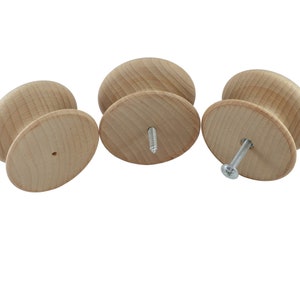 May include: Three wooden knobs with a round shape and a flat base. The knobs are unfinished and have a natural wood colour. One knob has a screw inserted into the base.