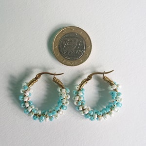 May include: A pair of hoop earrings made with blue and white beads. The earrings are about the size of a US quarter.