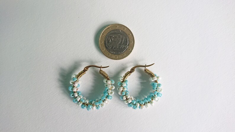 May include: A pair of hoop earrings made with blue and white beads. The earrings are about the size of a US quarter.