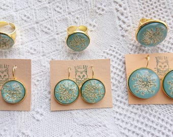 May include: Set of three gold rings and two pairs of earrings with delicate pressed flower designs in a light blue resin. The rings and earrings feature a gold metal setting.
