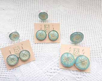 May include: Three sets of earrings and a ring with a light blue background and gold accents. The earrings are silver with a light blue background and gold accents. The ring is silver with a light blue background and gold accents. The earrings and ring are on a white background.