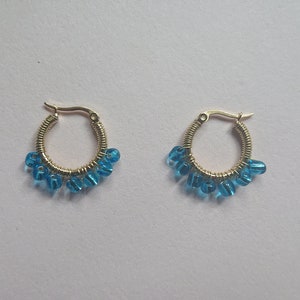 May include: A pair of gold hoop earrings with blue glass beads dangling from the bottom.