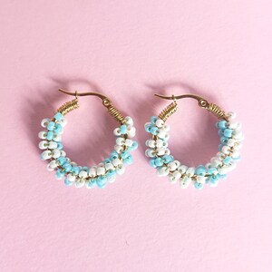 May include: A pair of gold hoop earrings with white and light blue beads. The beads are arranged in a spiral pattern.