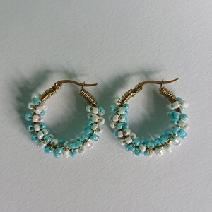 May include: A pair of hoop earrings with a gradient of blue and white beads. The earrings are made of gold-toned metal.