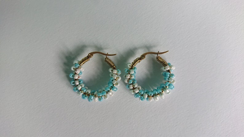 May include: A pair of hoop earrings with a gradient of blue and white beads. The earrings are made of gold-toned metal.