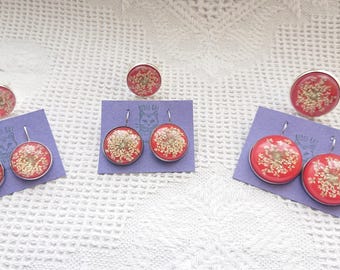 May include: Three sets of earrings and rings featuring pressed flowers encased in red resin. Each set includes a pair of earrings and a ring.