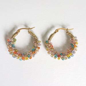 May include: A pair of gold hoop earrings with colorful beads. The beads are arranged in a spiral pattern around the hoop.