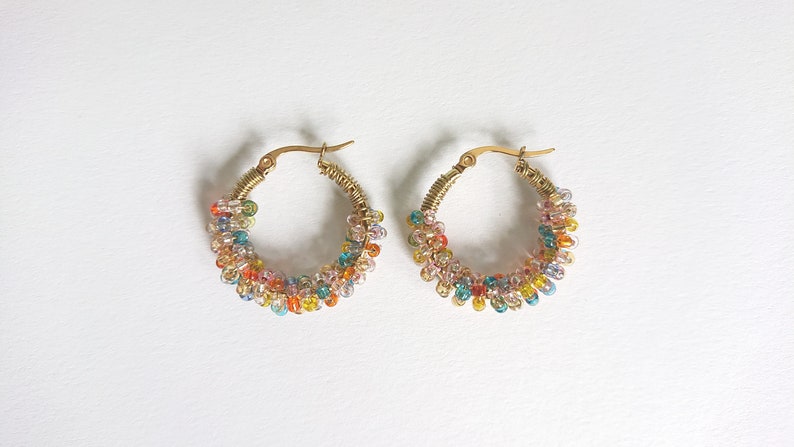 May include: A pair of gold hoop earrings with colourful beads. The beads are arranged in a spiral pattern around the hoop.
