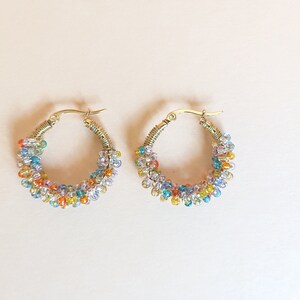 May include: A pair of gold hoop earrings with colourful beads. The beads are a mix of light blue, dark blue, orange, yellow, and white.