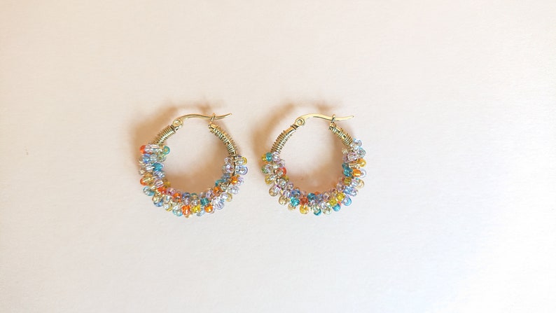 May include: A pair of gold hoop earrings with colourful beads. The beads are a mix of light blue, dark blue, orange, yellow, and white.
