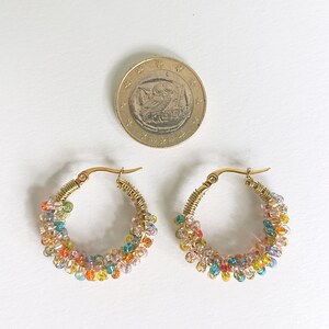 May include: A pair of gold hoop earrings with colourful beads. The beads are arranged in a spiral pattern around the hoop.