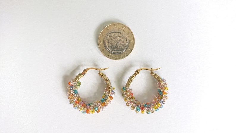 May include: A pair of gold hoop earrings with colourful beads. The beads are arranged in a spiral pattern around the hoop.