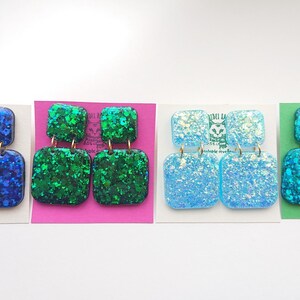 May include: Four pairs of square dangle earrings with glitter embedded in the resin. The earrings are in four colors: blue, green, light blue, and turquoise.
