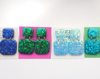 May include: Four pairs of square dangle earrings with glitter embedded in the resin. The earrings are in four colours: blue, green, light blue, and turquoise.