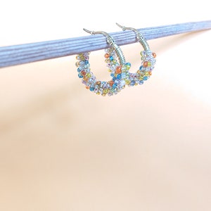 May include: A pair of silver hoop earrings with colourful beads. The beads are a mix of blue, green, yellow, orange, and white.