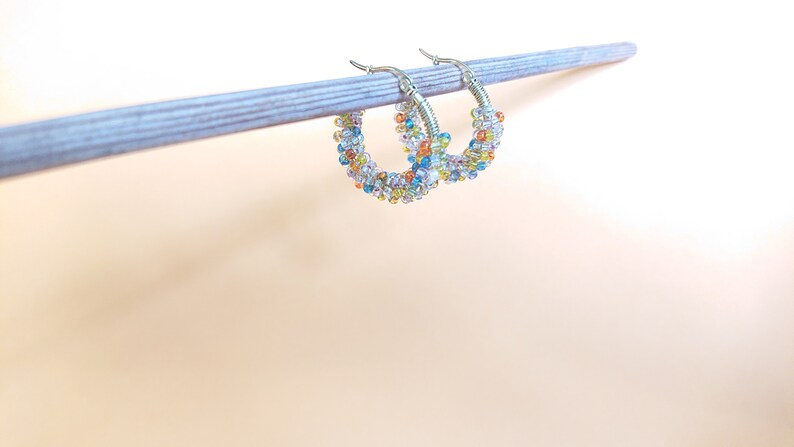 May include: A pair of silver hoop earrings with colourful beads. The beads are a mix of blue, green, yellow, orange, and white.