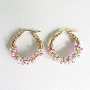 Pode incluir: Um par de brincos de argola dourados com contas coloridas. As contas s&atilde;o rosa, roxo, verde e branco.
