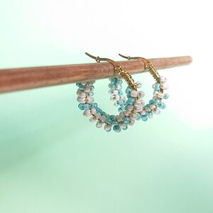 May include: A pair of gold hoop earrings with blue and white beads. The earrings are hanging from a wooden stick.