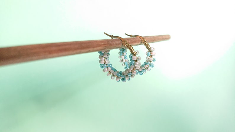 May include: A pair of gold hoop earrings with blue and white beads. The earrings are hanging from a wooden stick.