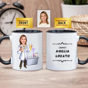 Könnte beinhalten: Weiße Keramiktasse mit schwarzem Rand und Henkel. Die Vorderseite der Tasse zeigt eine Cartoon-Illustration einer Person, die einen weißen Laborkittel trägt und ein Becherglas hält. Die Rückseite der Tasse trägt den Text "CHEMIST AMELIA LOVATO" in Schwarz.