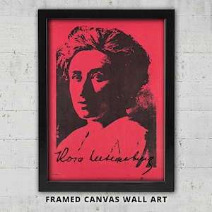May include: A framed canvas wall art piece featuring a high-contrast black portrait of Rosa Luxemburg set against a vibrant red background. The artwork includes the signature of Rosa Luxemburg in black script at the bottom of the portrait.