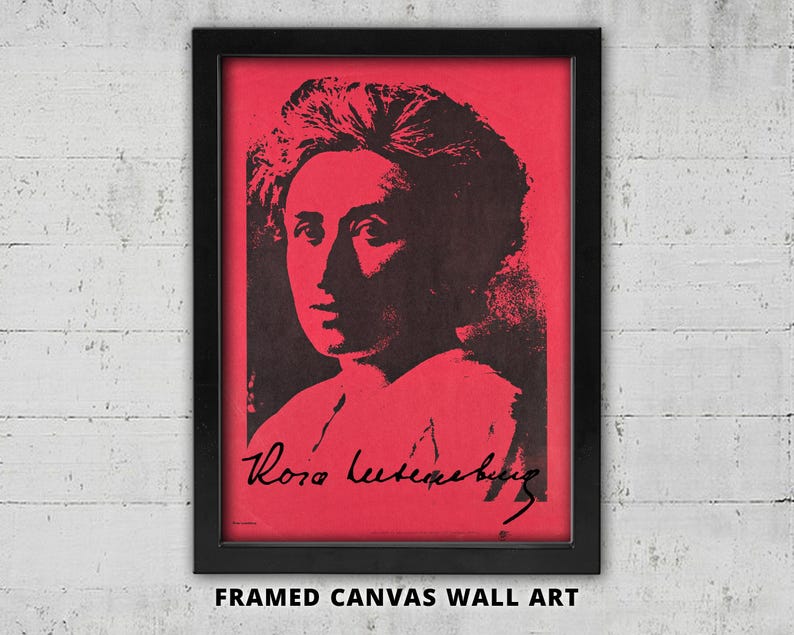 May include: A framed canvas wall art piece featuring a high-contrast black portrait of Rosa Luxemburg set against a vibrant red background. The artwork includes the signature of Rosa Luxemburg in black script at the bottom of the portrait.