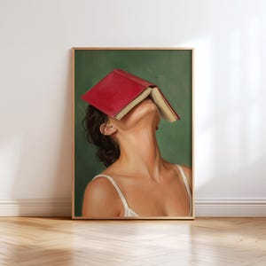Puede incluir: Una impresi&oacute;n art&iacute;stica enmarcada que presenta a una mujer con un libro rojo cubriendo su rostro, sobre un fondo verde. La mujer lleva una camiseta blanca. La obra de arte est&aacute; en un marco de madera y se exhibe en una pared.