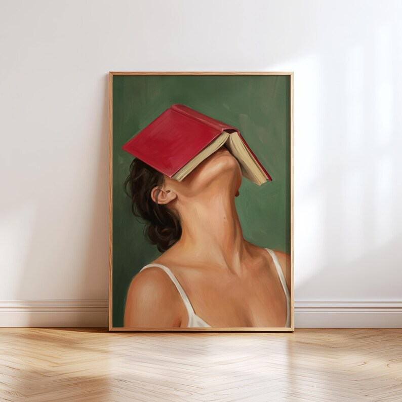 Puede incluir: Una impresi&oacute;n art&iacute;stica enmarcada que presenta a una mujer con un libro rojo cubriendo su rostro, sobre un fondo verde. La mujer lleva una camiseta blanca. La obra de arte est&aacute; en un marco de madera y se exhibe en una pared.