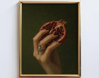 Könnte beinhalten: Ein gerahmter Kunstdruck, der eine Hand mit dunkelrotem Nagellack zeigt, die einen halbierten Granatapfel vor einem dunkelgrünen Hintergrund hält. Die Hand trägt einen silbernen Schlangenring um einen Finger, eingefasst in einen dünnen Goldrahmen.