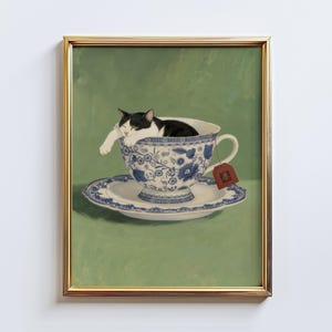 May include: A framed print showing a black and white cat asleep in a blue and white floral teacup. The teacup rests on a matching saucer, with a tea bag tag attached. The background is a solid green.