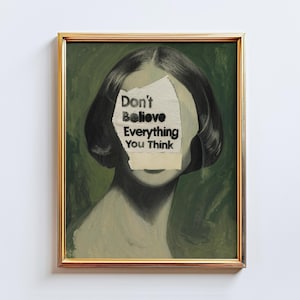 May include: Framed art print. The portrait depicts a person with a section of their face covered by paper bearing the text "Don't Believe Everything You Think." The artwork is set in a gold frame against a green backdrop.