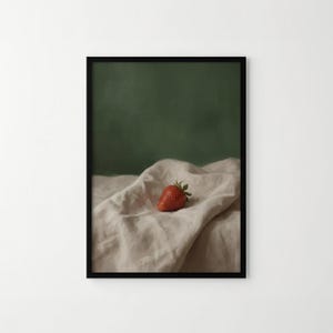 Puede incluir: Una impresi&oacute;n art&iacute;stica enmarcada que presenta una fresa madura. La fruta roja se encuentra sobre una tela beige texturizada, con un fondo verde oscuro. La obra de arte tiene una calidad suave y pict&oacute;rica, evocando calma y simplicidad.