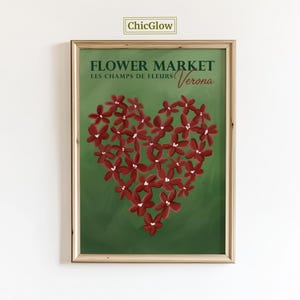 Op de afbeelding: Een ingelijste kunstdruk met een hartvormige opstelling van bordeauxrode bloemen op een groene achtergrond. De tekst "FLOWER MARKET" en "Verona" worden weergegeven, samen met "LES CHAMPS DE FLEURS". Het kunstwerk zit in een houten lijst.