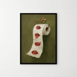 Op de afbeelding: Een ingelijste kunstdruk met een rol toiletpapier met geschilderde rode lippen op elk vel. Het kunstwerk is gemonteerd op een messing toiletpapierhouder tegen een groene achtergrond. De lippen hebben verschillende uitdrukkingen.